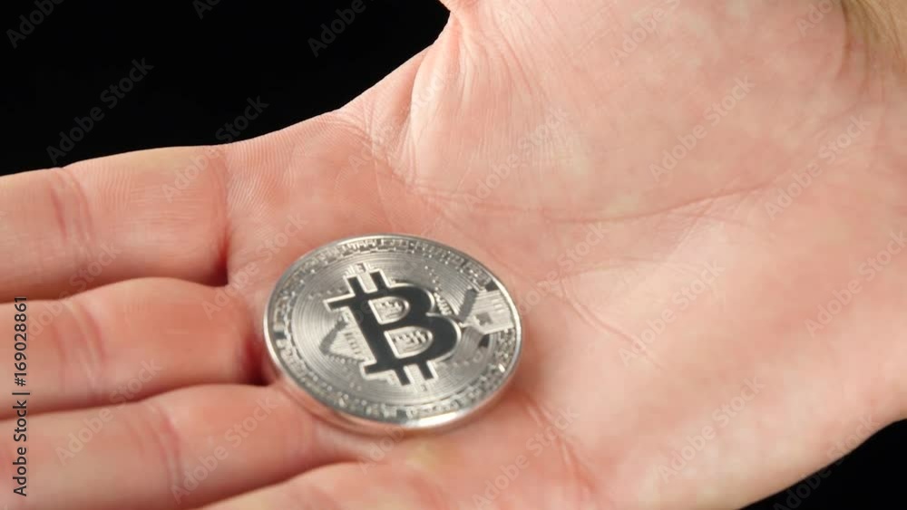 Silver Bitcoin in a man's hand. Symbol of a new virtual currency . Silver Bitcoin in a man's hand. Symbol of a new virtual currency .