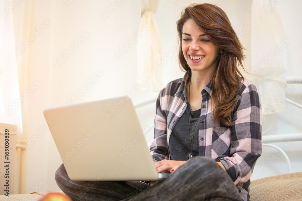Fototapeta premium Young woman sitting on sofa and using laptop at home.