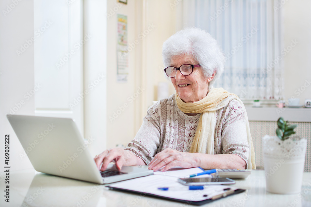 Modern elderly woman using laptop and calculating bills at home. Modern elderly woman using laptop and calculating bills at home.