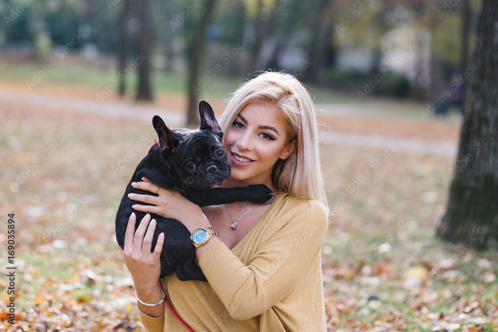 Beautiful and happy young blond woman enjoying in autumn park with her adorable French bulldog puppy. Beautiful and happy young blond woman enjoying in autumn park with her adorable French bulldog puppy.