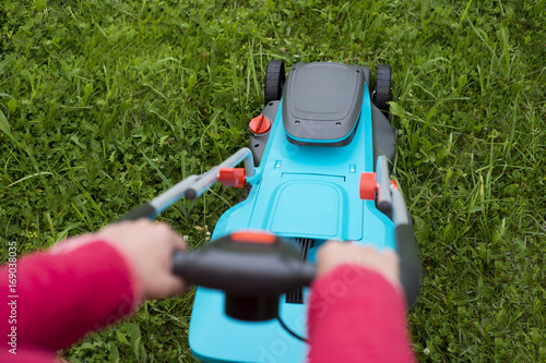 Woman mowing the lawn with blue lawnmower in summertime - close up