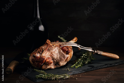 Freshly roasted lamb leg with herbs and bottle of red wine