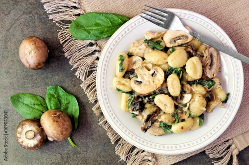 Gnocchi with a mushroom cream sauce, spinach, chicken and sun dried tomatoes, above scene on a dark stone background