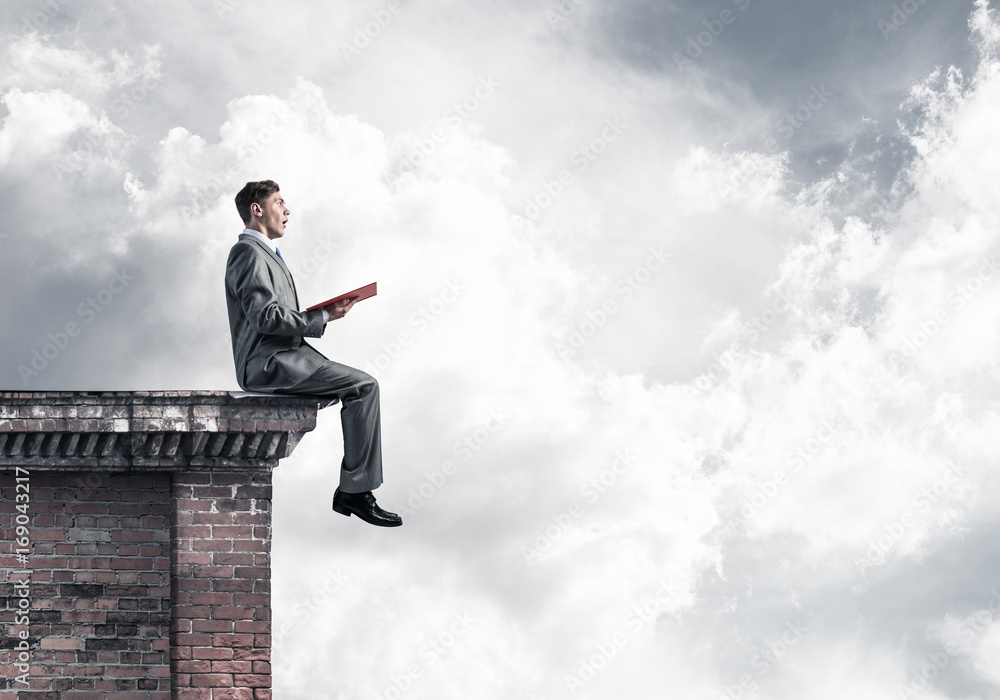 Man on roof edge reading book and cloudscape at background Man on roof edge reading book and cloudscape at background
