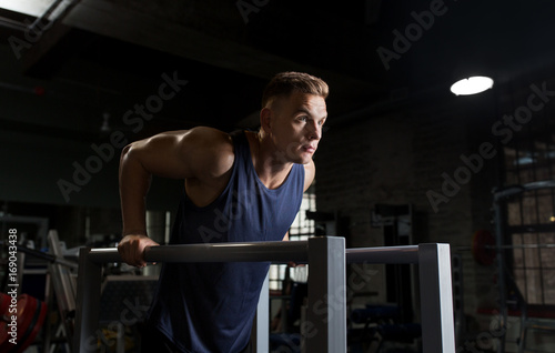 man doing triceps dip on parallel bars in gym