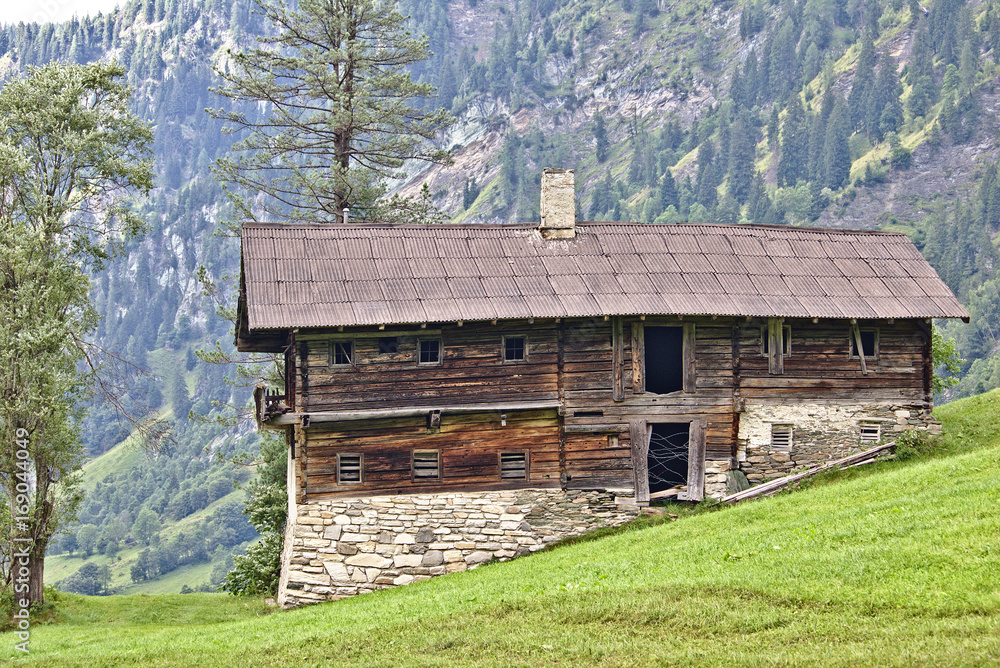 Derelict wooden farmhouse with field stone foundations and timber walls on a grassy slope