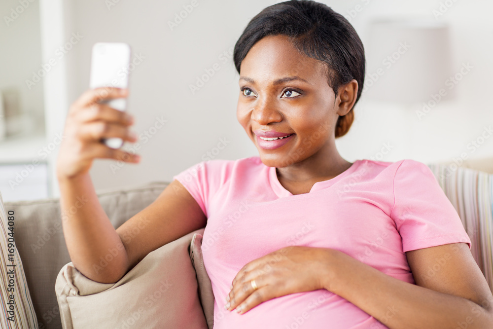 pregnant woman taking smartphone selfie at home