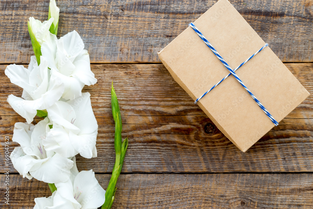 Gift box wrapped in craft paper near flower gladiolus on rustic wooden background top view copyspace Gift box wrapped in craft paper near flower gladiolus on rustic wooden background top view copyspace