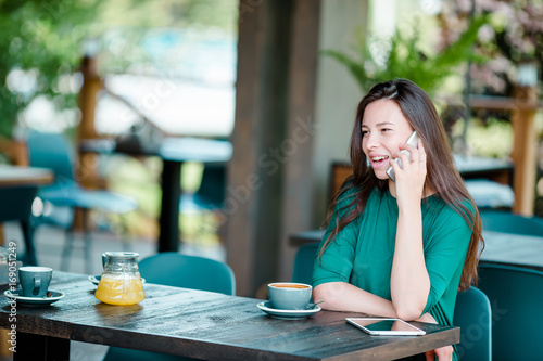 Young woman calling with cell telephone while sitting alone in coffee shop during free time. Attractive female with cute smile having talking conversation with mobile phone while rest in cafe