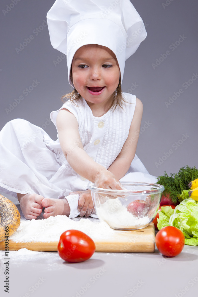 Food Concepts and Ideas. Funny Smiling Little Caucasian Girl In Cook Uniform Preparing Courses With Flour and Vegetables In Studio Environment.