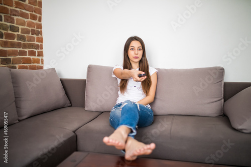 Happy young woman watching tv on sofa at home