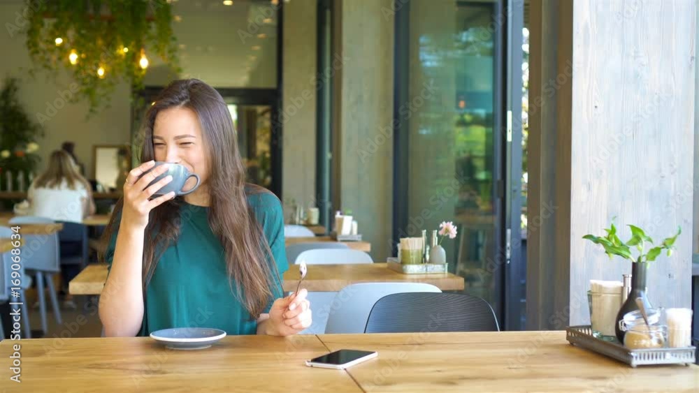 Young woman calling with cell telephone while sitting alone in coffee shop during free time. Attractive female with cute smile having talking conversation with mobile phone while rest in cafe Young woman calling with cell telephone while sitting alone in coffee shop during free time. Attractive female with cute smile having talking conversation with mobile phone while rest in cafe