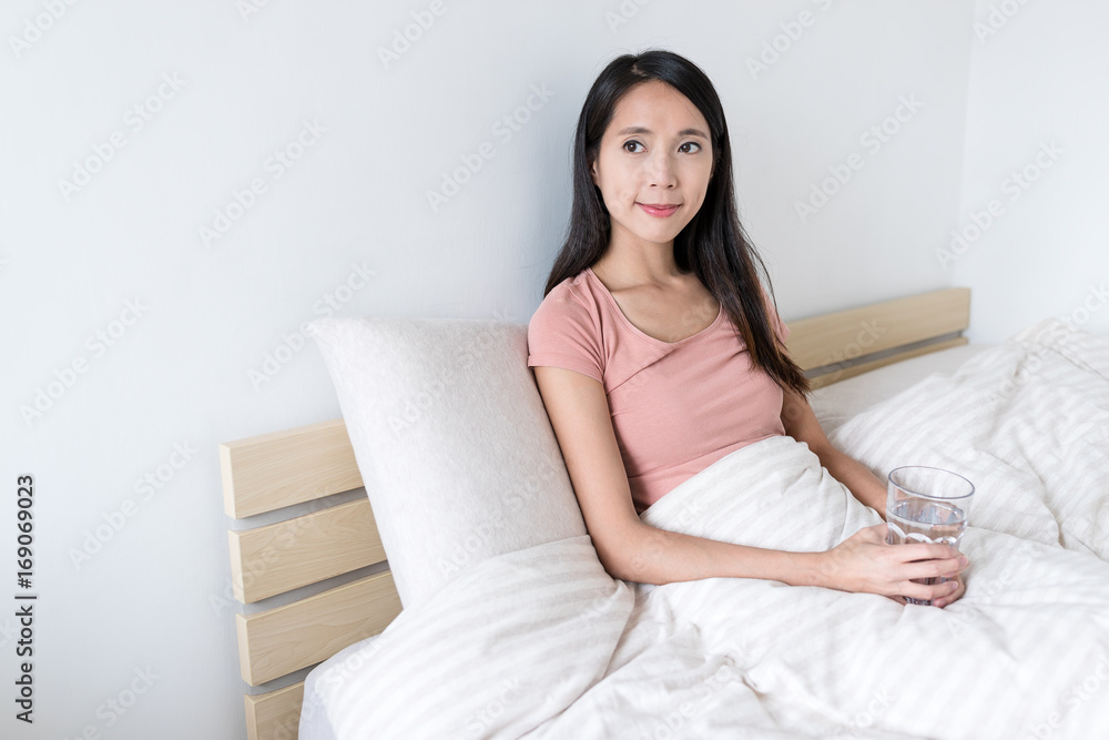 Woman holding glass of water and looking of out window in bedroom Woman holding glass of water and looking of out window in bedroom