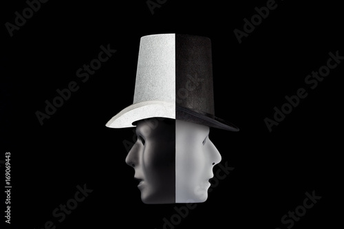 Black and white masks wearing top hat looking in opposite directions isolated on black background with copy space. Double talk and hypocricy concept photo