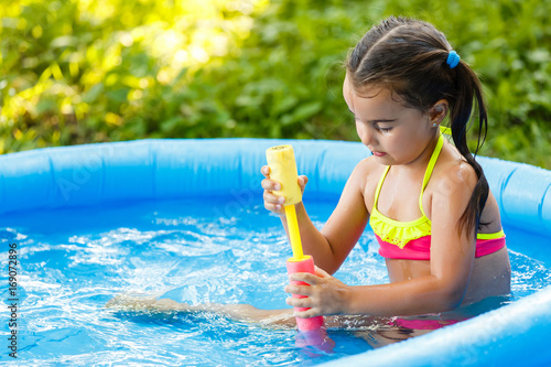 little girl with water sprayer by swimming pool photo