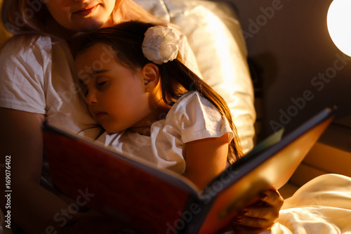 Foto Little daughter fell asleep at mom while reading book