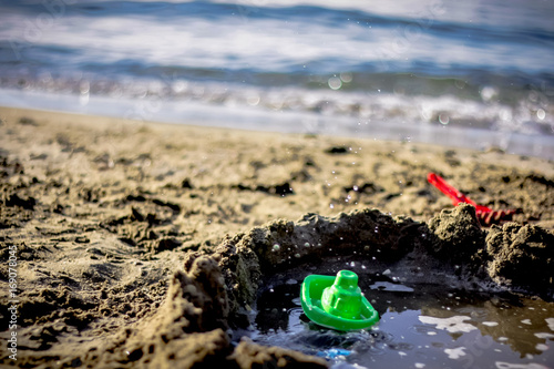 A little green toy boat on the beach .