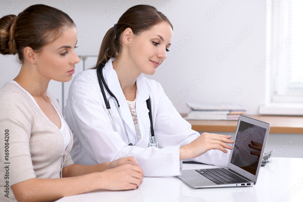 Doctor and patient sitting at the desk. Physician pointing into laptop computer. Medicine and health care concept Doctor and patient sitting at the desk. Physician pointing into laptop computer. Medicine and health care concept