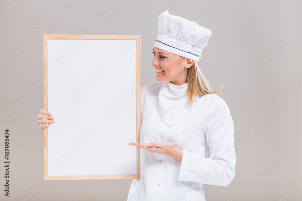 Portrait of beautiful female chef showing whiteboard on gray background. Portrait of beautiful female chef showing whiteboard on gray background.