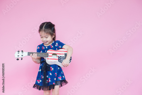 Little beautiful asian girl playing guitar on pink background with copy space