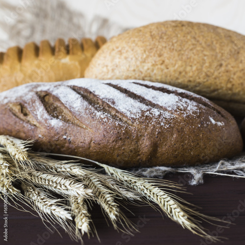 Rye, grain and white bread next to the spikelets of rye on a wooden table