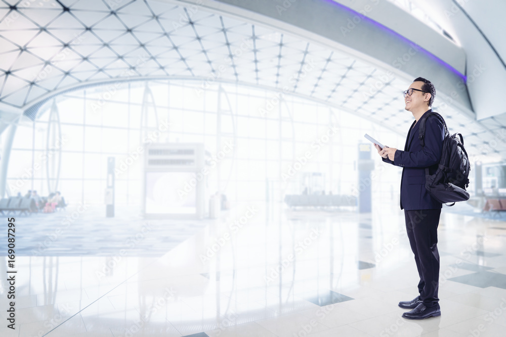 Young business man using digital pad smiling happy inside airport waiting hall . Young business man using digital pad smiling happy inside airport waiting hall .