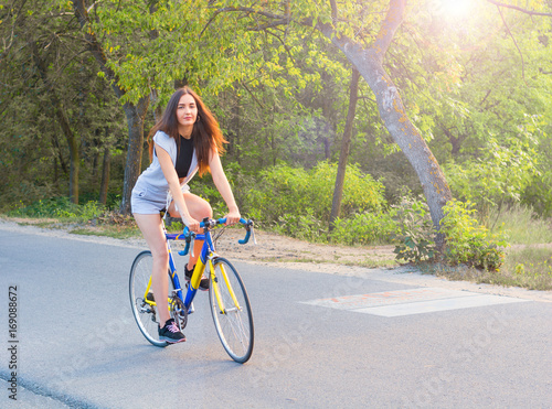 Young woman rides on a bicycle on the road in the park in the sunset rays of the sun