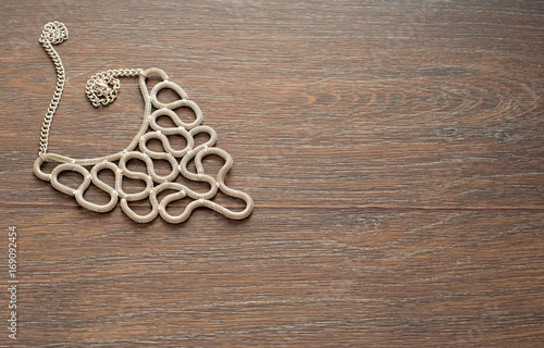 Metal necklace for women on brown wooden background.