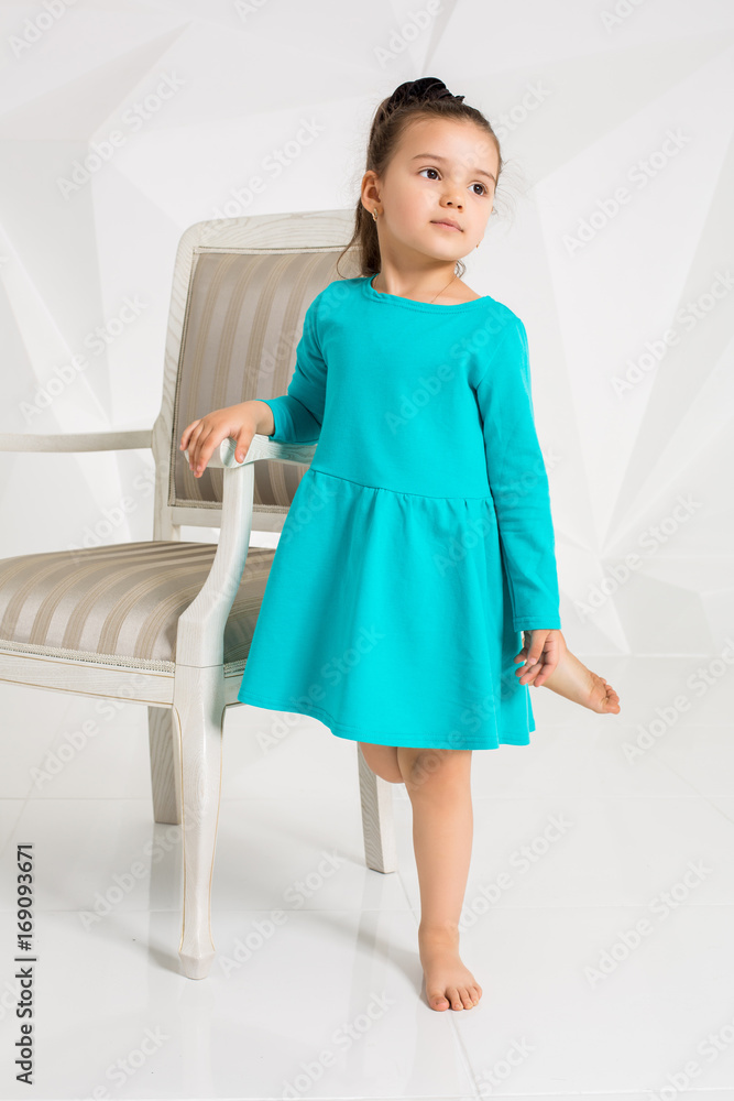 Beautiful little girl in a turquoise dress posing in front of camera in studio Beautiful little girl in a turquoise dress posing in front of camera in studio