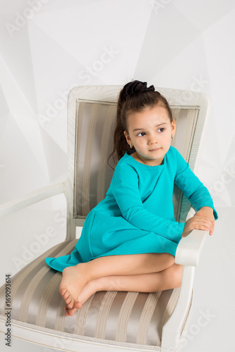 Beautiful little girl in a turquoise dress posing in front of camera in studio