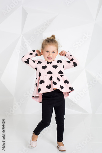 Beautiful little girl in a pink tunic with black hearts and leggings posing in front of camera in studio photo