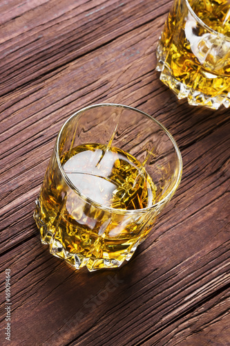 Whisky with ice in two glasses on a wooden background