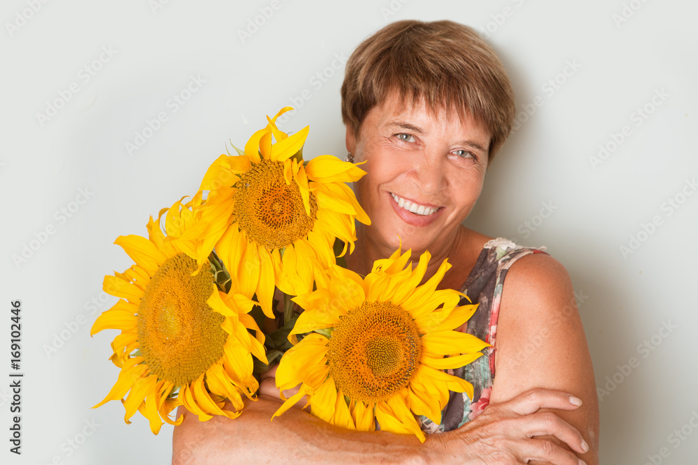 Fototapeta premium Happy elderly woman with a sunflower on a gray background