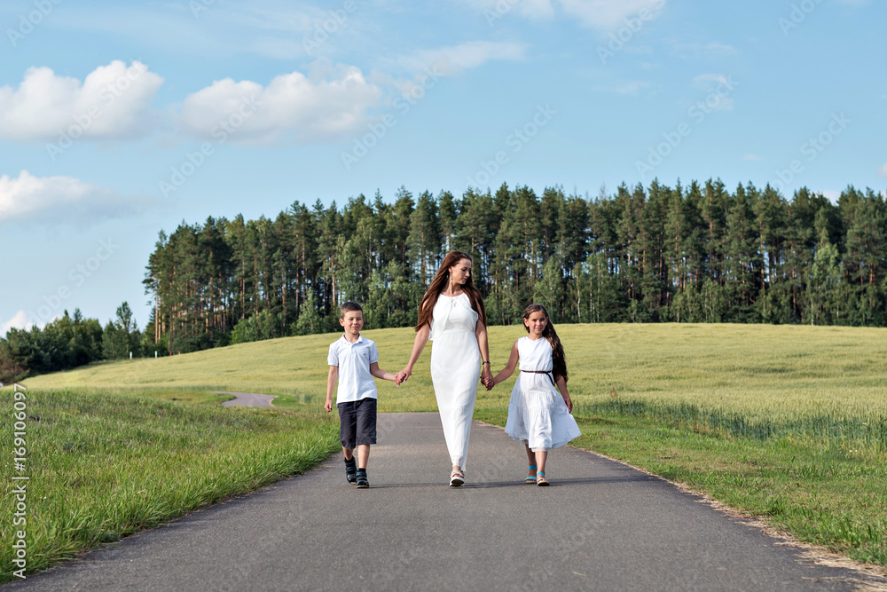 Family mom and two children girl and boy walking on the road in the park among the wheat fields and forests Family mom and two children girl and boy walking on the road in the park among the wheat fields and forests