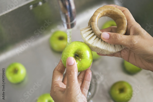 Young Vegan Girl Washing Green Apples with Bamboo Brush. Hand Holding Fresh Fruits Under Running Water in Kitchen Sink. Healthy Lifestyle Hygiene Concept. photo