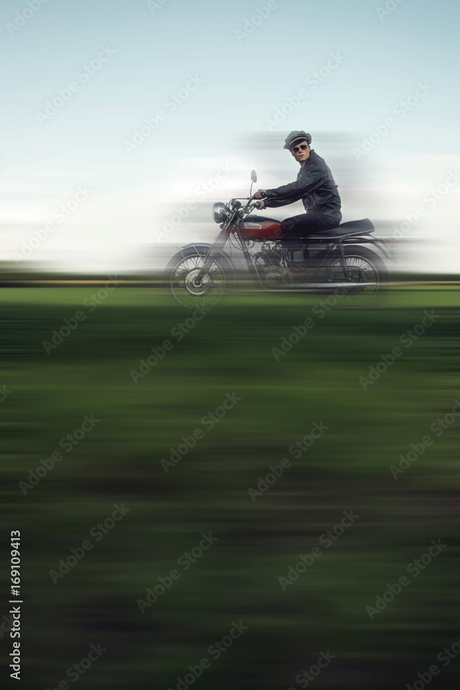 Vintage motorcyclist riding in summer countryside landscape.