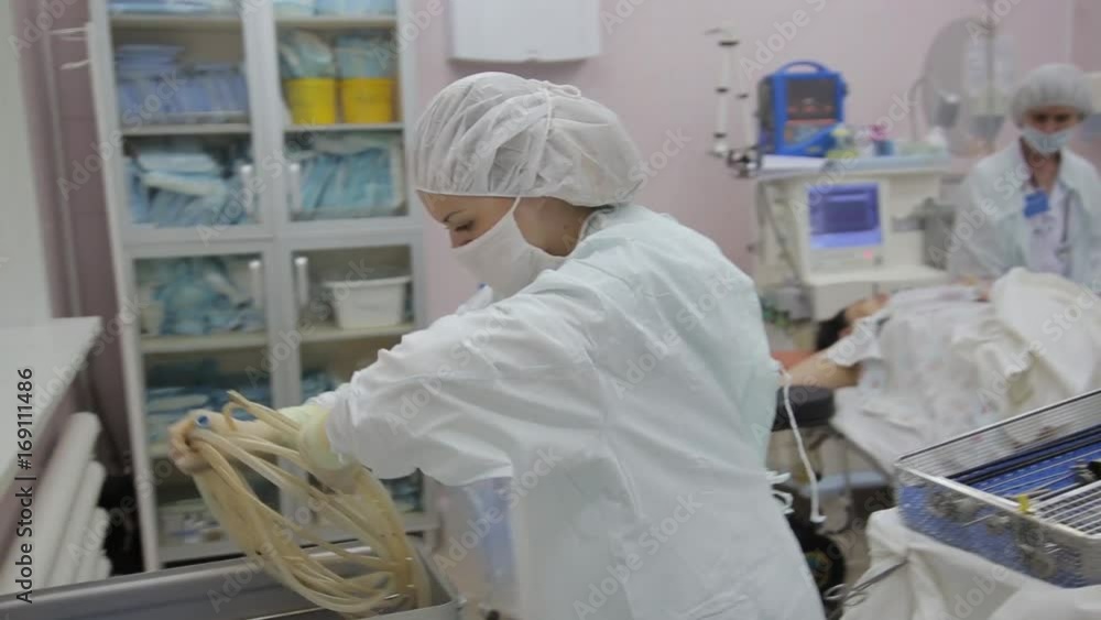 A female surgeon assistant moves the surgical instruments into a container A female surgeon assistant moves the surgical instruments into a container