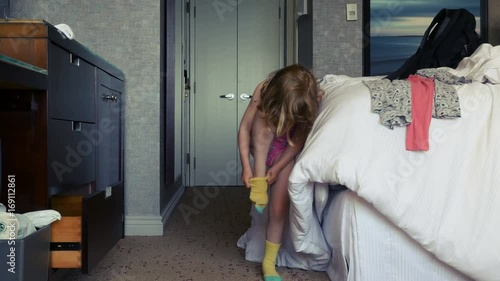 A little girl gets dressed. She tries to put on a yellow sock and walks away. Long shot.