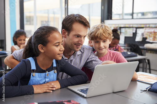 Teacher and two young students use laptop computer in class