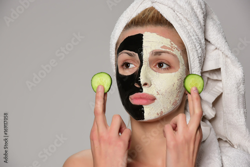 beautiful female model with black and white facial cosmetic mask posing. Isolated on gray background.