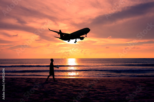 silhouette man walikng on the beach during airplane is landing at airport photo