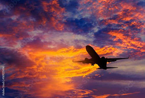 Fotografie Silhouette passenger airplane flying away in to sky high altitude during sunse