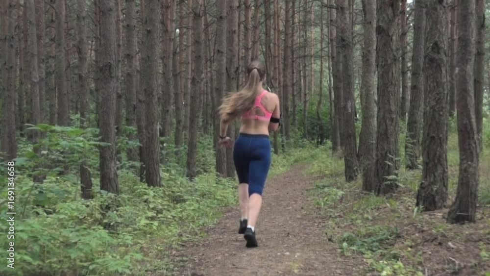 Woman athlete running in the forest, back view, slow motion Woman athlete running in the forest, back view, slow motion