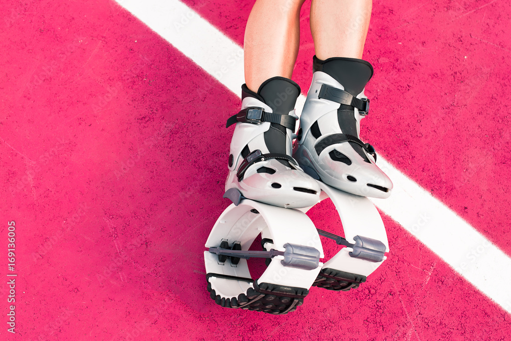 Fit legs in kangoo jumping shoes. Beautiful and sexy girl do sport kangoo  exercises on pink background and sit Stock Photo