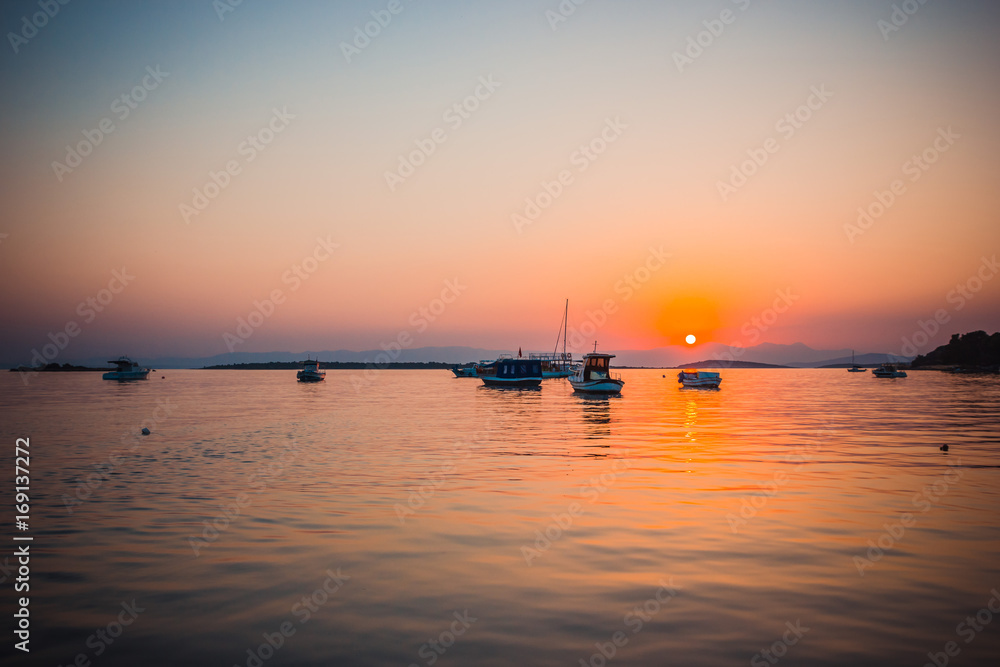 Naklejka premium Boats in the sea at sunset in summer with mountains on background
