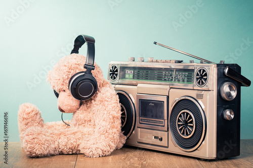 Retro radio recorder from 80s and toy Teddy Bear with headphones in front mint background. Vintage style filtered photo