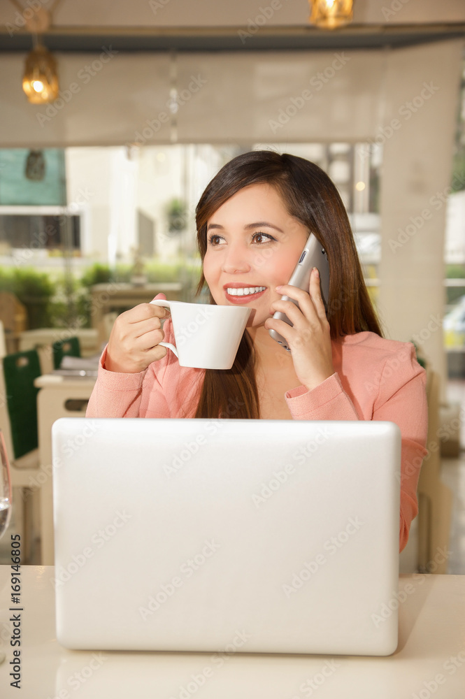 Close up of a young beautiful businesswoman working and drinking coffe while she is using her cellphone to make a call. Business concept Close up of a young beautiful businesswoman working and drinking coffe while she is using her cellphone to make a call. Business concept