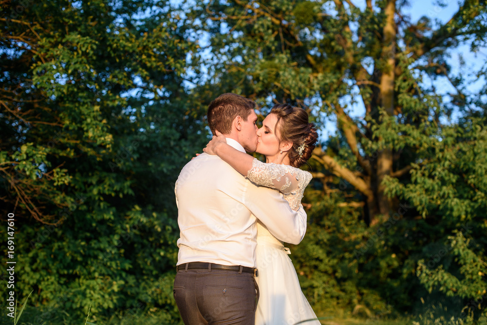 Bride and groom kissing and holding hands in the forest on nature