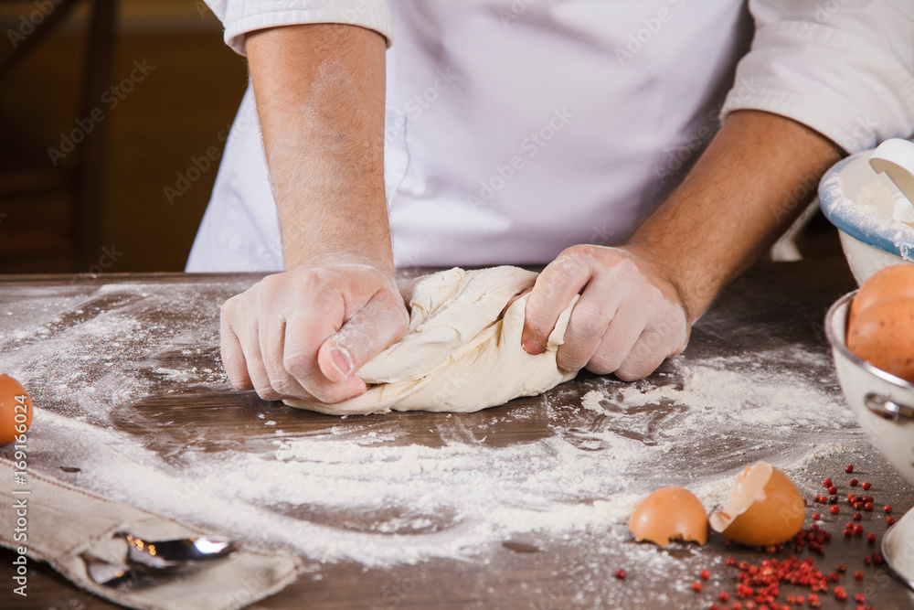 The chef kneads the dough on the kitchen table with his hands.