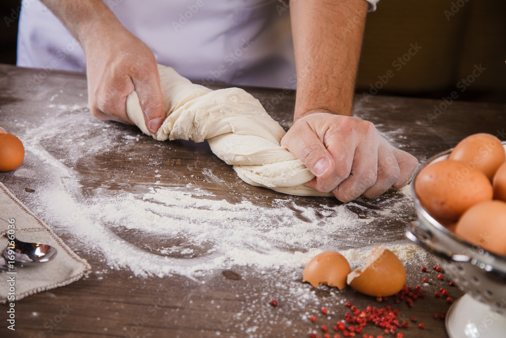 The chef kneads the dough on the kitchen table with his hands.